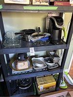 Shelf with various kitchen items including bakeware, frying pans, a fondue pot, glass and metal bowls, and the Keurig coffee maker.