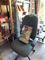 Photo of green fabric office chair with black armrests and caster wheels; oversized chair cover box placed on the seat.