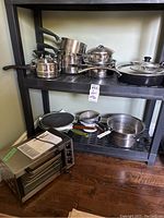 Photo showing the Hamilton Beach toaster oven with manual placed on a shelf alongside assorted pots, pans, and Dutch ovens of stainless steel and non-stick varieties.