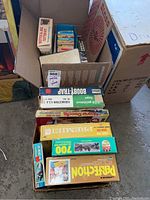Two open boxes showing various boxed puzzles, board games, games and toys stacked inside. Box top view shows titles clearly including Booby Trap, Magna Doodle and Perfection.