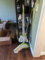 Steam mop and broom set shown assembled and standing together on wooden floor, with mop pads and manual visible.