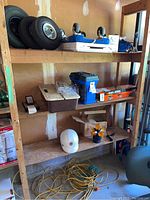 Wood shelf holding three trailer tires, dolly stool with blue padding and caster wheels, toolboxes, and Black and Decker trimmer box.