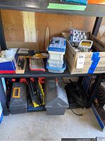 Shelf with various toolboxes, containers of drill bits, extension cord, and hand tools boxed in Rubbermaid and black toolboxes