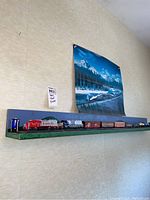 Full view of 10 model trains arranged on a two-tone wooden shelf mounted on wall with train poster above