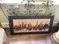Framed city skyline painting against a pegboard wall showing abstract cityscape in muted tones