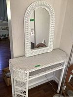 Full view of white painted wicker vanity with a rectangular top surface and open shelf below, setup against a wall.