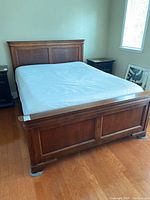 Full view of queen size wooden bed frame from front showing headboard, footboard, and mattress.