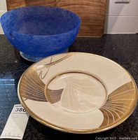 Two bowls on countertop: blue glass bowl and beige ceramic bowl with gold details.