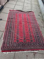 Full view of red patterned carpet showing the overall design and damage, including edge wear and fraying.