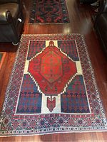 View of largest carpet showing overall condition, design, and colors in a living room setting between two leather chairs on wooden flooring.