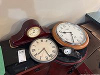 Four clocks of various sizes and styles arranged on furniture showing different shapes and designs.