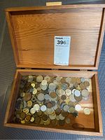 Wooden box with coins spread out inside showing a variety of coins and sizes.
