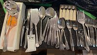 Wide view of various cutlery pieces including forks, spoons, and knives with patterned handles, some loose and some boxed small spoons.