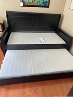 Hasselvika black day bed with white mattress and instruction manual sitting on the mattress