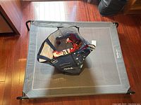 Overview image showing the Bedsure elevated dog bed on a wooden floor with a tote bag of assorted pet toys placed on top.