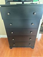 Front view of black 5-drawer storage cabinet dresser with round knobs on each drawer.