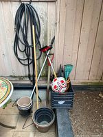 Photo of the lot showing the garden hose hanging on wall, plant pots on floor and a black crate containing gardening tools and the soccer ball.