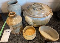 Five handcrafted pottery items displayed on countertop: two jars, one covered oval casserole, and two small bowls.