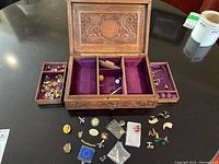 Open carved wood jewelry box on table showing four removable trays and assorted contents