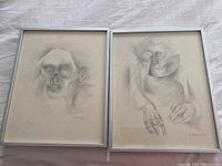 Two framed pencil drawings placed side by side on fabric surface, showing full artwork and frames.
