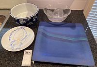 Overview of plates and bowls including a white bowl with blue floral design, clear divided glass bowl, square blue plate, and round decorative plate with Jean Cocteau artwork.
