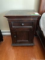 Front view of one dark wood side table showing drawer above a cabinet door with knob handles.