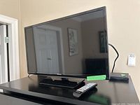 Samsung 28 inch TV on black stand with remote placed on the stand.