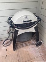 Front view of Weber Q natural gas grill on cart stand with hose connected