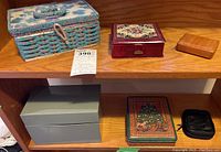 Top shelf containing floral wicker sewing box, burgundy wooden box with floral tapestry, and small light wooden box