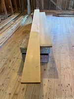 Two long lumber boards placed parallel on a stand inside a wooden floor room. One is lighter pine and the other darker cedar.