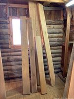 Multiple rough sawn maple lumber boards approximately 2x6 in size and various lengths placed upright against a wall in a wooden building interior.