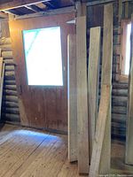 Multiple maple wood planks leaning against a wall near a window and door inside a wooden structure.