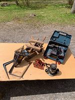 Top view of lot items arranged on table outdoors showing Bosch drill in case, vintage wood clamps, metal lantern, animal trap, router, and angle brackets