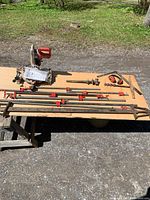 Full view of table displaying the power saw, multiple bar clamps, auger bits, square, vice screw, and earmuffs