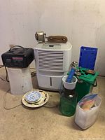 Overview showing Frigidaire dehumidifier, battery charger on top of a metal bucket, kitchen composter, plexiglass shooting target stand, lawn chair webbing rolled up, several decorative plates and glass containers
