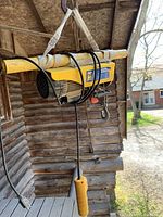 Electric yellow cable hoist hanging from wooden beam, showing cable, hook and controller