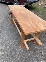 Angled view showing full maple hardwood bench top with two wooden bench dogs and metal vice on left side.