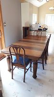 Full view of the dining table with four chairs around it, showcasing the large wooden table with distinct wood panel patterns and turned legs.