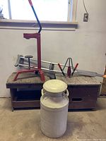 Milk can, crutches, and wine corking equipment arranged on wooden furniture under window with electrical outlet.