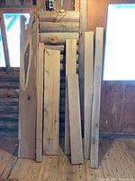 Several hardwood lumber boards standing upright against rustic wooden wall in indoor setting, showing various widths and lengths, natural finish.
