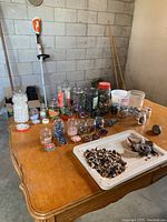 Photo showing a large variety of polished stones and minerals arranged in jars and bowls on a wooden table, including clear quartz, sodalite, tiger eye, amethyst, and others.