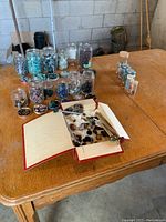 Lot of assorted polished gemstones in glass jars and laid on table, along with small jewelry pieces scattered inside a box