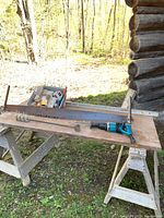 Overview of lot on wooden boards held by saw horses, outdoors with natural light, showing crosscut saw, reciprocating saw, and metal level.