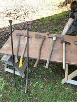Full view of all tools on a wooden table outdoors showing prybars, axes, sledgehammer, and adze.