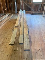Seven rough sawn pine lumber boards stacked on a wood floor, showing different thicknesses likely 2x4 and 2x6 dimensions.