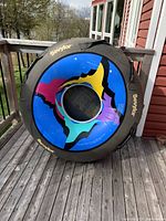 Photo of the round ski tube showing the colorful inside and the black Sevylor-branded cover from the side, placed on a wooden deck with outdoor background.