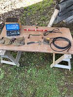 Photo of socket set, nail belts, level, drill bits, hand tool, and extension cords on wooden table outdoors.