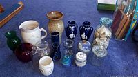 Photo of assorted glass and pottery vases and jars showing various shapes and colors on a dark surface.