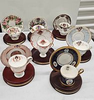 Eight Avon Honor Society collectible teacup and saucer sets displayed on dark wooden stands with engraved plaques showing different years.
