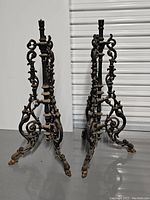 Pair of antique cast iron table bases with detailed scroll designs and tripod claw foot legs shown from front angle.
